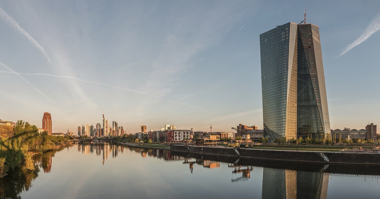 The European Central Bank skyscraper in Frankfurt at dawn, with the Main river in the foreground and the financial skyline in the background