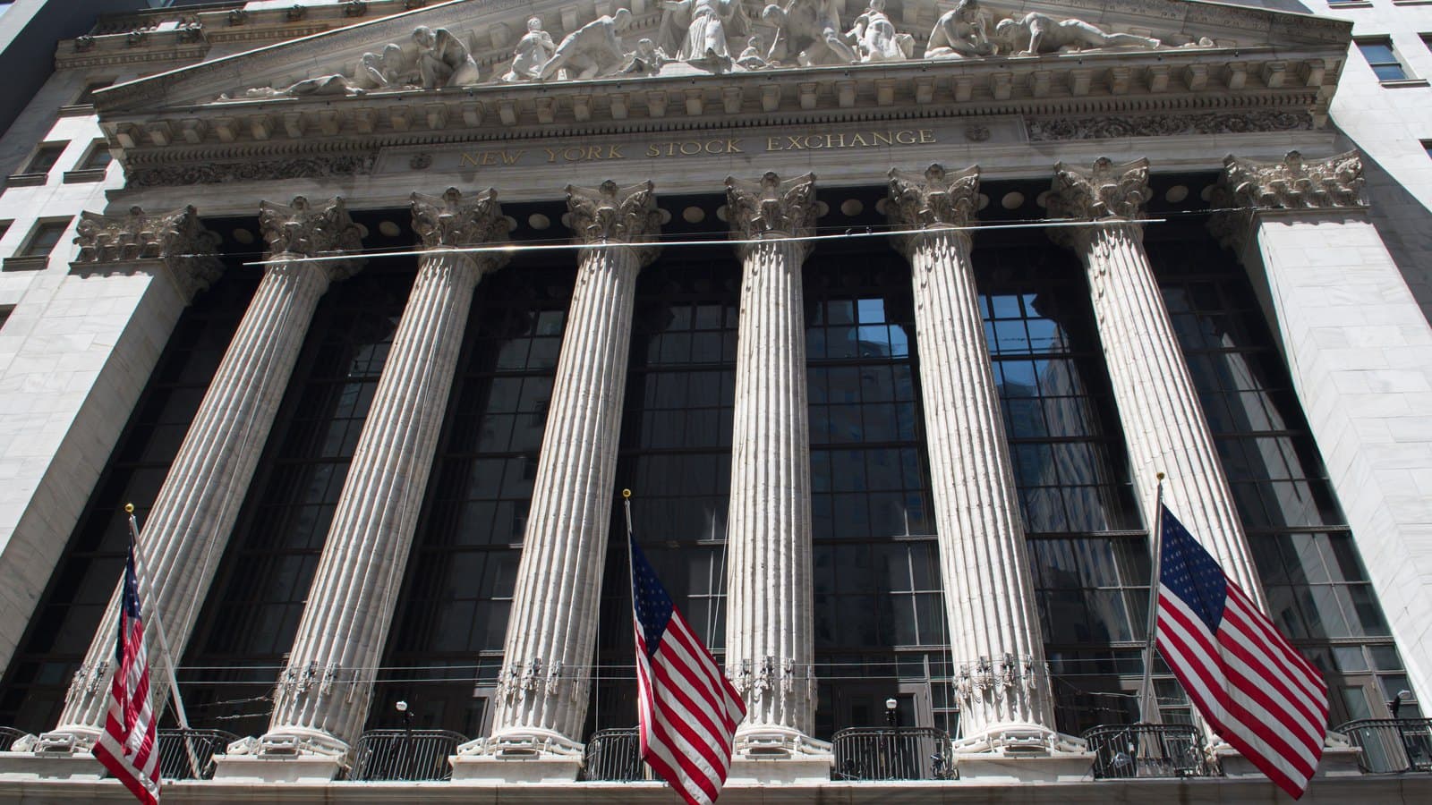 The neoclassical facade of the New York Stock Exchange on Wall Street, with Corinthian columns and three American flags